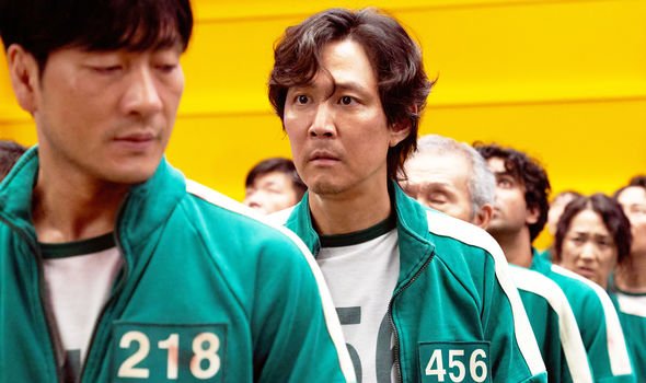 A picture containing player 456 in his green jumpsuit standing in line behind Player 218
